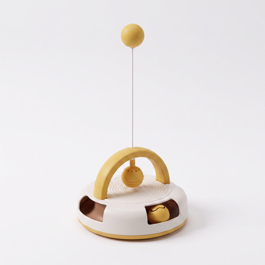 Eddy Gravity Feather Spinner cat toy shown from a three-quarter rear angle, revealing the mustard-yellow arch handle, hanging ball teaser, and the side track windows with interactive balls on the white ripple-top base