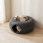 Two cats share the FELVO Burrow felt tunnel nest, one asleep on top and one looking out of the tunnel