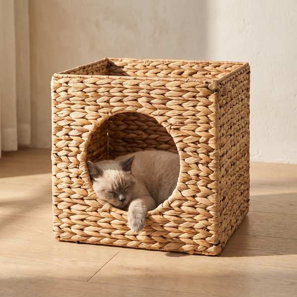 A cat sleeps inside the FELVO Willow woven water hyacinth cat cave on a pale oak floor