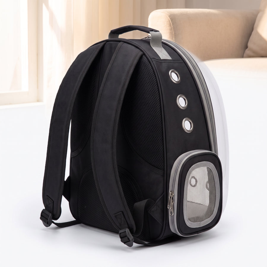 Vista Clear Cat Backpack, empty carrier shown from a three-quarter rear angle, revealing the padded shoulder straps, ventilated back panel, silver grommet vents, and side mesh pocket on the black and grey shell with clear bubble dome