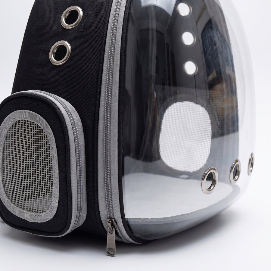 Close-up detail of the Vista Clear Cat Backpack showing the clear bubble dome seam, silver grommet air vents, and zipper stitching on the black and grey carrier shell